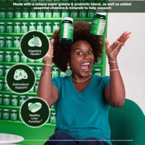 Mujer feliz sosteniendo frascos de Goli Supergreens frente a una pared de productos, señalando beneficios digestivos y antioxidantes.